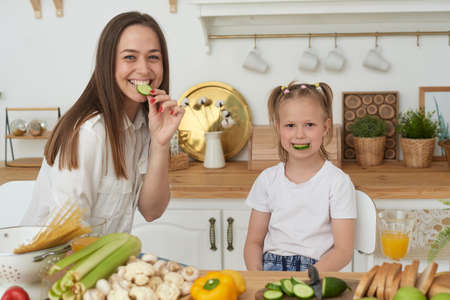 Healthy food at home. A cheerful mother laughs, has fun and hugs her daughterの写真素材