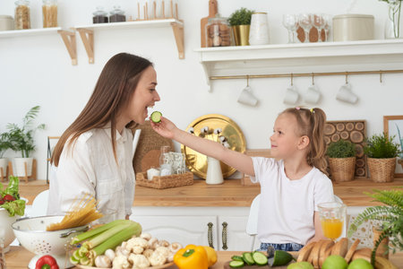 Mom and daughter are eating cucumbers and laughing. Proper nutrition at home. Spending time togetherの写真素材