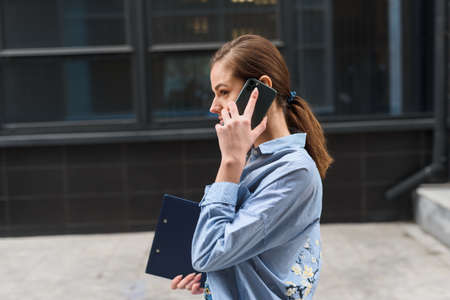 A businesswoman walks against the backdrop of an office center and speaks on the phone....