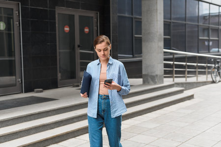 Young stylish female businesswoman leaves the office center and looks at the phone. The concept of feminism and womens businessの写真素材