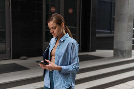 Young stylish female businesswoman leaves the office center and looks at the phone. The concept of feminism and womens businessの写真素材