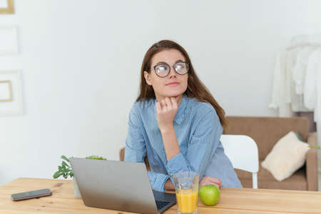 Pensive student girl sit in front of laptop thinking over task . Young concerned woman deep in their thoughts frown searching issue problem, hesitate to make business decision having doubts in accessing work situation.の写真素材
