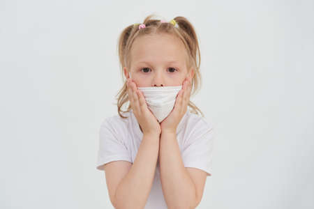 A frightened little girl in a protective mask looks at the camera.の写真素材