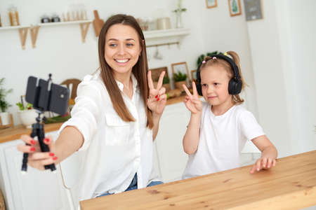 Mom and daughter show peace gesture to the camera. Writing a blog to a video platformの写真素材