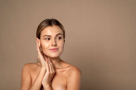 Skin care. Woman with beauty face touching healthy facial skin. Beautiful smiling Caucasian female model with natural makeup touching glowing hydrated skin on beige backgroundの写真素材
