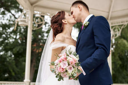 The bride and groom are kissing in the open. Focus on the bouquet. Wedding, love and youth conceptの写真素材