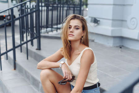 Portrait of an attractive happy woman sitting on the stairs in a city street and looking at the...