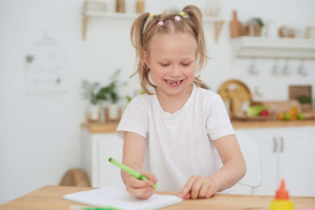 Cute little smiling girl enjoys studying and doing homework at home in the kitchen. Independent workの写真素材
