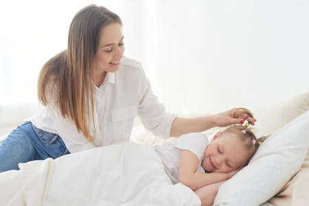 Beautiful young mom wakes up her preteen little daughter in the morning. Tenderness and care. Mothers loveの写真素材