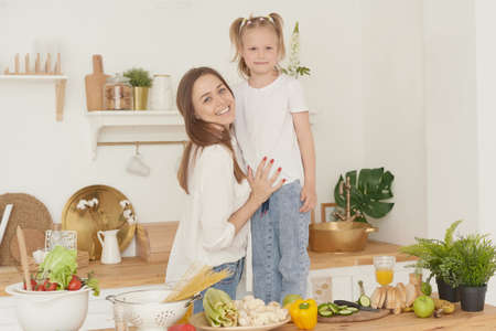 Mom and daughter are standing in the kitchen of the house, looking at the camera and laughing. Proper nutrition at home. Spending time togetherの写真素材