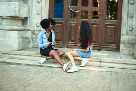 Happy young african american woman smiling enjoy fun conversation with indian friend, mixed race teen girl talk laughing outdoor conceptの写真素材