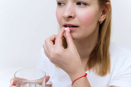 Young woman with glass of water taking sleeping pills and not feeling well in bed, copy space. Using medical drug at home. Vitamin or supplementの写真素材