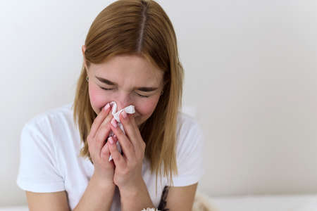 Sick millennial woman feeling bad, weak fight against flu, runny nose, rest at home, health problem concept. The woman blows her nose into a handkerchief. depression, sadness and cryingの写真素材
