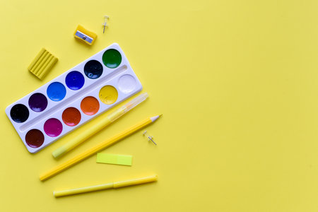 Paint, pencils and scissors. School accessories on a yellow background. View from aboveの写真素材