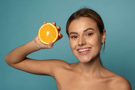 Attractive caucasian female with clean skin laughing with closed eyes and showing half of fresh orange while advertising benefits of vitamin Cの写真素材