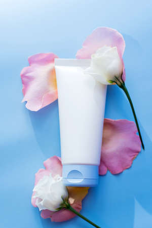 Mock-up cream in a white package on a blue background next to rose petalsの写真素材