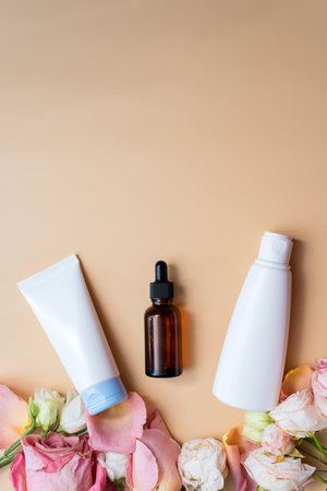 Mock-up cream and lotion in white packages and moisturizing serum in a brown glass bottle on a blue background next to rose petals. The concept of creating natural cosmeticsの写真素材