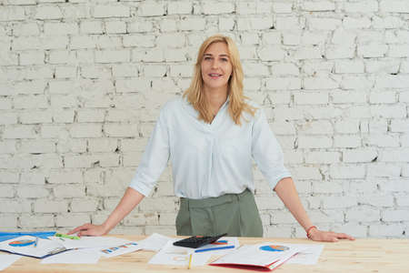 A business woman stands at a table with business reports and looks into the camera. Copy spaceの写真素材
