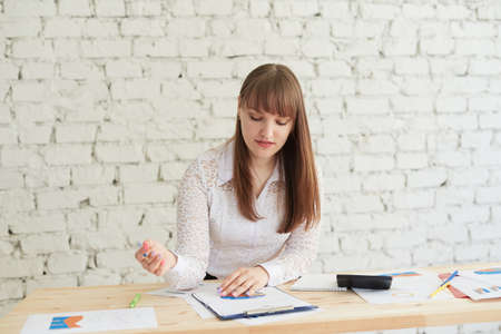 Beautiful young woman in elegant casual wear looking at chart while standing in officeの写真素材