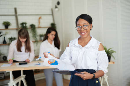Happy smiling woman looks at charts and work papers in the office against the background of the female teamの写真素材
