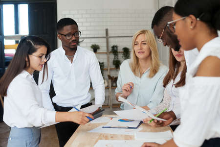 A team of multiethnic people are discussing business in the office. The employees of the company communicate, looking at the schedules and discussing the further strategyの写真素材