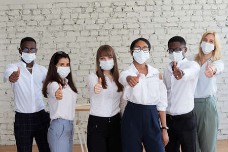 Quarantine, back to work concept. Confident multicultural businessmen standing in office wearing protective medical masks looking at camera.の写真素材