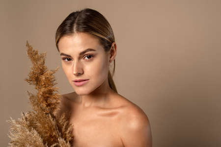 A beautiful young woman with her hair pulled back holds a dry pampas grass in her hands. The concept of natural cosmetics from wheat grains. Skin careの写真素材