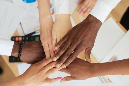 Close-up top view: multinational employees put their hands in a pile, showing support and unity, together towards a common goal. Successful teamの写真素材