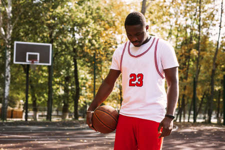 Portrait of a handsome black young man holding a basketball on a basketball court. Take a break during your workout. Fashionable sports portraitの写真素材