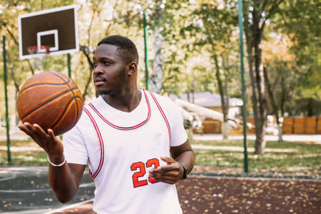 Young black smiling man playing basketball on the court at sunrise, morning sports. Outdoor portraitの写真素材