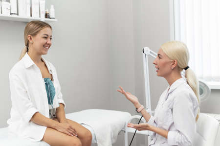 A female cosmetologist consults a female client in a beauty clinic. Beautician prepares patient for spa skin care procedure by talking about skin treatmentの写真素材