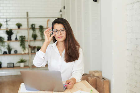 A beautiful young Afghan woman in elegant business attire sits in front of a table at a laptop with charts and graphsの写真素材