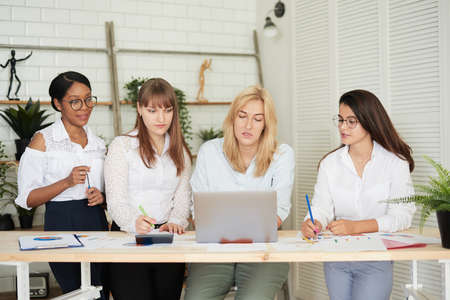 Smiling women work together in a modern office. Feminism. Professional smiling business women standing in the office and discussing business papersの写真素材