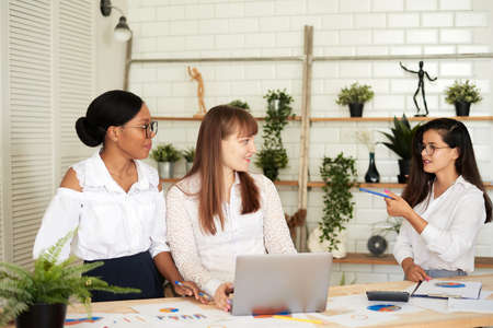 Smiling women work together in a modern office. Feminism. Professional smiling business women standing in the office and discussing business papersの写真素材