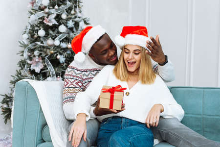 A woman is surprised by the gift that her husband gave her. Couple Sharing Christmas Present. Portrait of lovely couple in christmas timeの写真素材