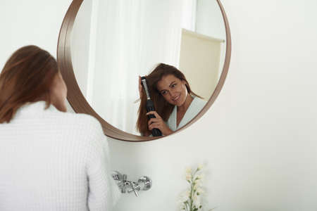 A woman winds her hair with a hairdryer in the bathroom. Beautiful lady does her hair at homeの写真素材