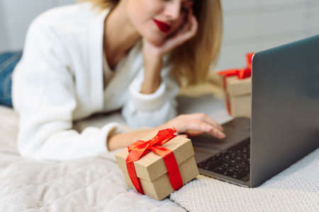 Women wearing white sweater lying on the sofa and using laptop to shopping online at home. christmas online shopping conceptの写真素材