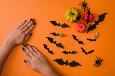 Halloween black manicure, hand skin care, spa salon. October discounts. Female hands on an orange background with decorative pumpkins, bats and spidersの写真素材