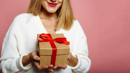 Caucasian young woman in santa hat showing red gift box and smiling isolated on pink background. Happy New Year celebration merry holiday concept. Close up. Web bannerの写真素材