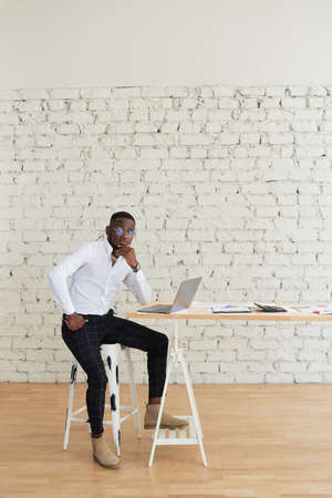 Smiling African man working at home sitting at the table. Concept of young people using laptopの写真素材
