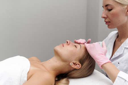 Beautician or masseur doing manual relaxing rejuvenating face and neck massage for young woman in...