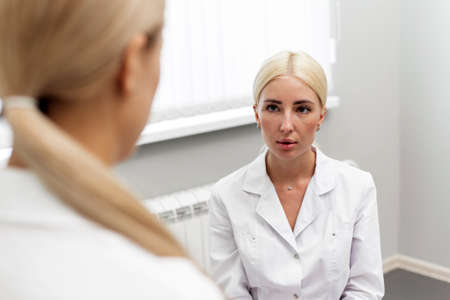 A female cosmetologist consults a female client in a beauty clinic. Beautician prepares patient for spa skin care procedure by talking about skin treatmentの写真素材