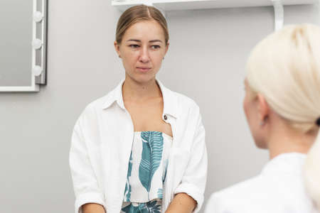 A female client looks at a young doctor in a beauty parlor. Consultation with a beautician before the skin care procedure. Cosmetology and beauty conceptの写真素材
