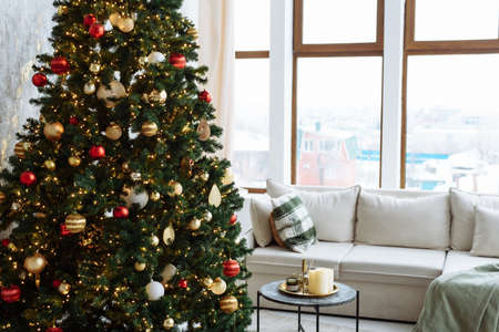 Christmas tree with red and gold balls and gold garland lights in a bright room.