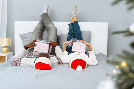 Joyful couple together in bed on Christmas morning. Caucasian woman and African American man celebrate Christmas togetherの写真素材
