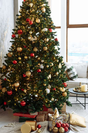 Christmas tree with red and gold balls and gold garland lights in a bright room.の写真素材