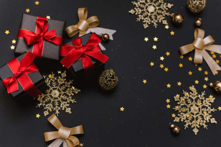 Black Christmas gifts with red bows on a black background with gold snowflakes and decorations. Flat lay, copy spaceの写真素材