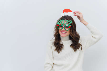 Woman in white sweater wearing santa hat and glasses 2022 on white isolated backgroundの写真素材