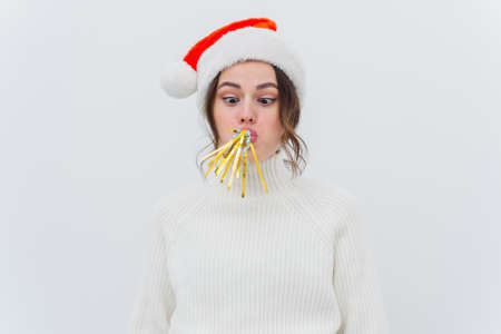 Young woman in santa hat blowing festive pipe isolated on white background.の写真素材