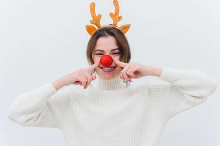 Photo of an overjoyed funny lady in a christmas deer costume and a white sweater with a red bauble and a white backgroundの写真素材